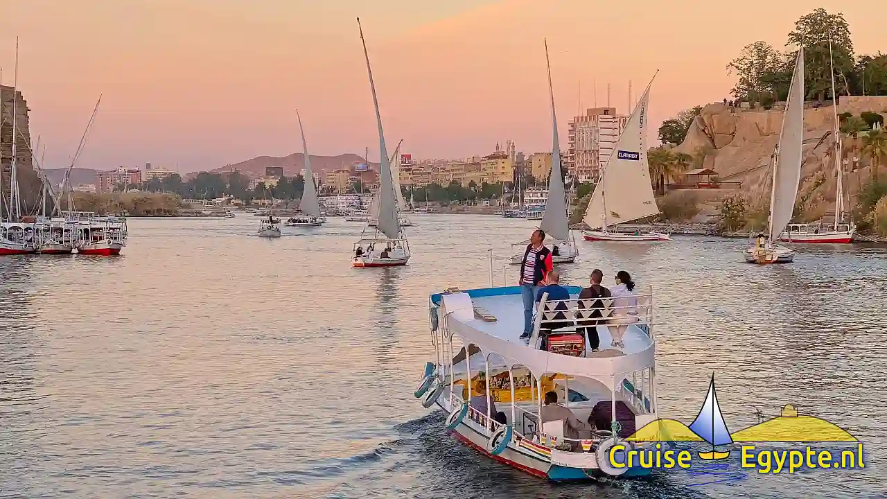 Motorboot met passagiers op het bovendek tussen zeilende feloeken op de Nijl bij Aswan, in het avondlicht